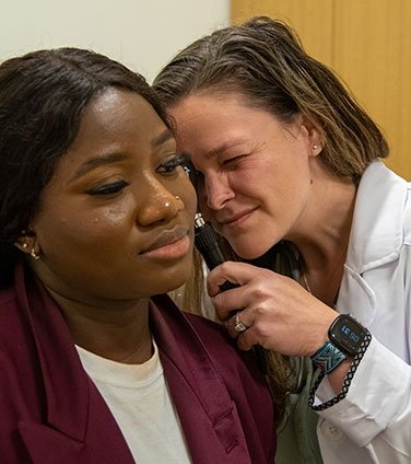 Nursing student looks in the ear of a patient