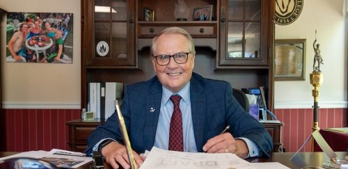 President Warner smiling as he writes at his desk