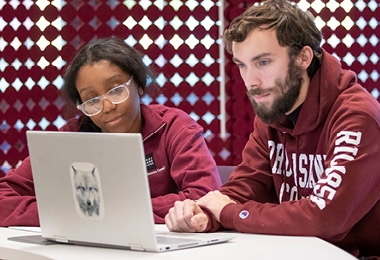 Two students working together at a laptop, one student in RIC sweatshirt