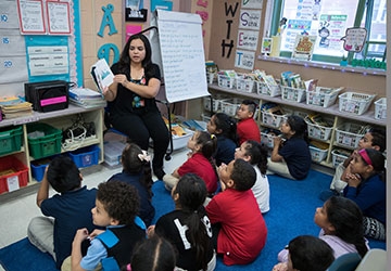 Education student reads to students sitting on a rug