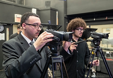 Two communication students looking through video cameras