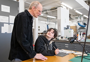 Art student working, with faculty looking at the work