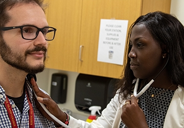 Nusing student in medical coat with stethoscope, listening to the breathing of a patient