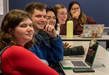 Smiling, engaged students in class at tables with laptops