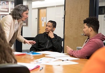 Students working around a table with a professor guiding them