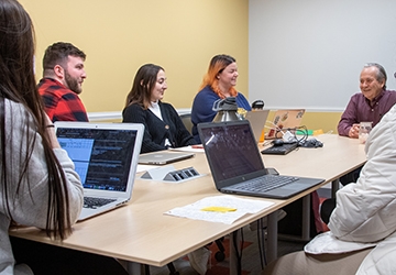 Students working together around a table with laptops