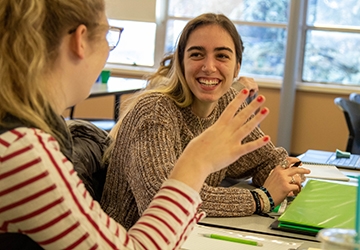 Two students in animated classroom conversation, smiling and gesturing