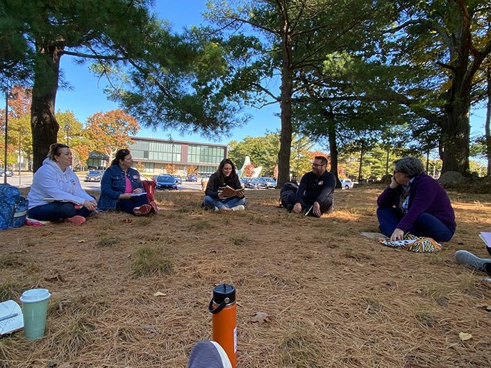 People sitting under trees on campus, sharing their writing