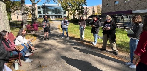 People on campus, standing in a circle, with writing supplies