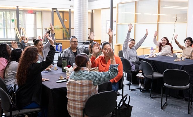 Social work students listening to speaker and raising hands enthusiastically